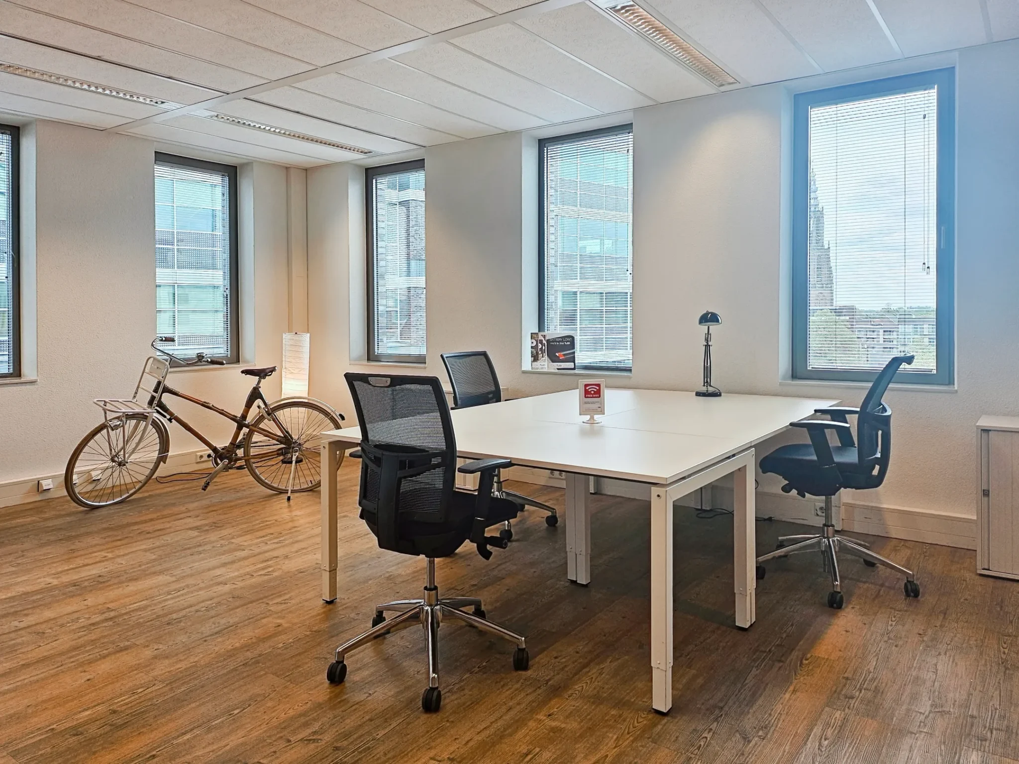 Moderne kantoorruimte met houten vloer, witte bureaus, ergonomische stoelen en een vintage fiets tegen de muur.