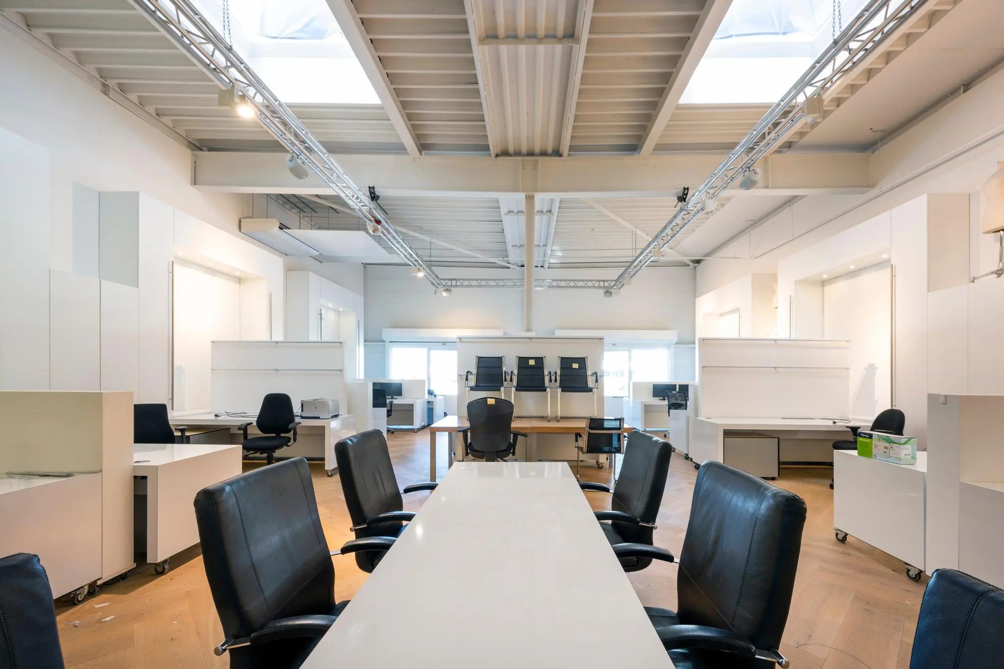 Modern, licht kantoorinterieur met lege bureaus, zwarte bureaustoelen en een lange vergadertafel.