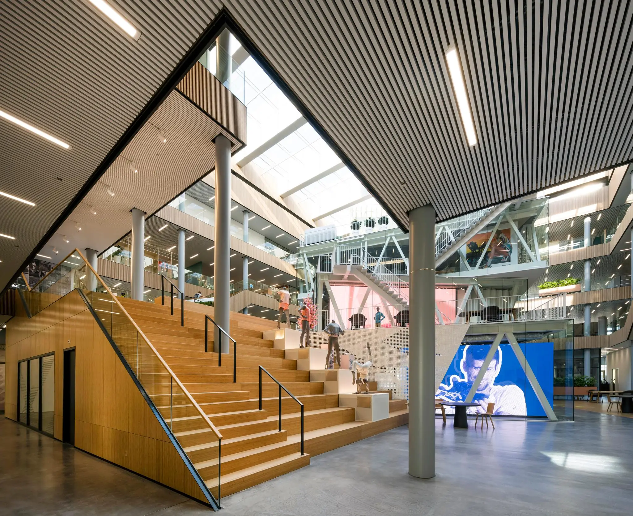 Moderne, open kantoorruimte in Taurusavenue met houten trappen, sculpturen en grote digitale schermen.