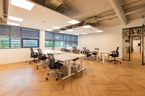 Moderne kantoorruimte met bureaus en stoelen, omgeven door grote ramen en houten vloeren.