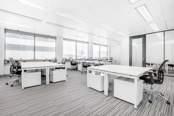 Een moderne, lichte kantoorruimte met bureaus, stoelen en computers.