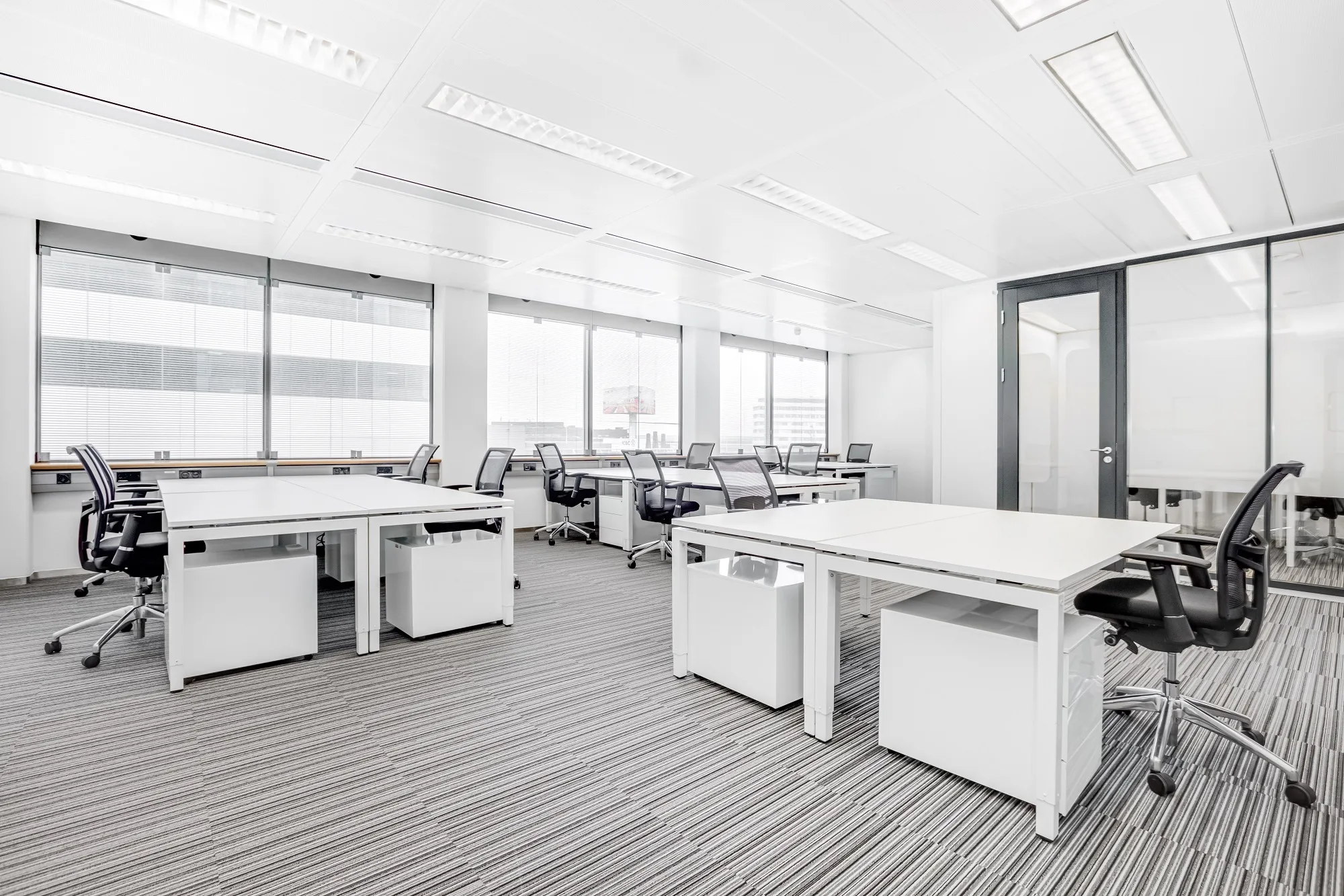 Een moderne, lichte kantoorruimte met bureaus, stoelen en computers.