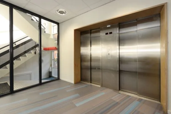 Moderne lifthal met twee roestvrijstalen liften en een glazen wand met zicht op een trap in gebouw Spui.