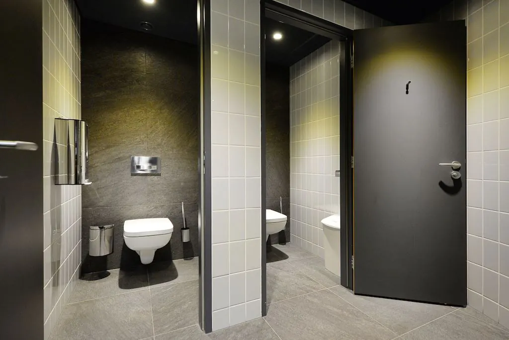 Moderne openbare toiletruimte met twee betegelde toiletcabines, elk voorzien van een hangtoilet en hygiënevoorzieningen.