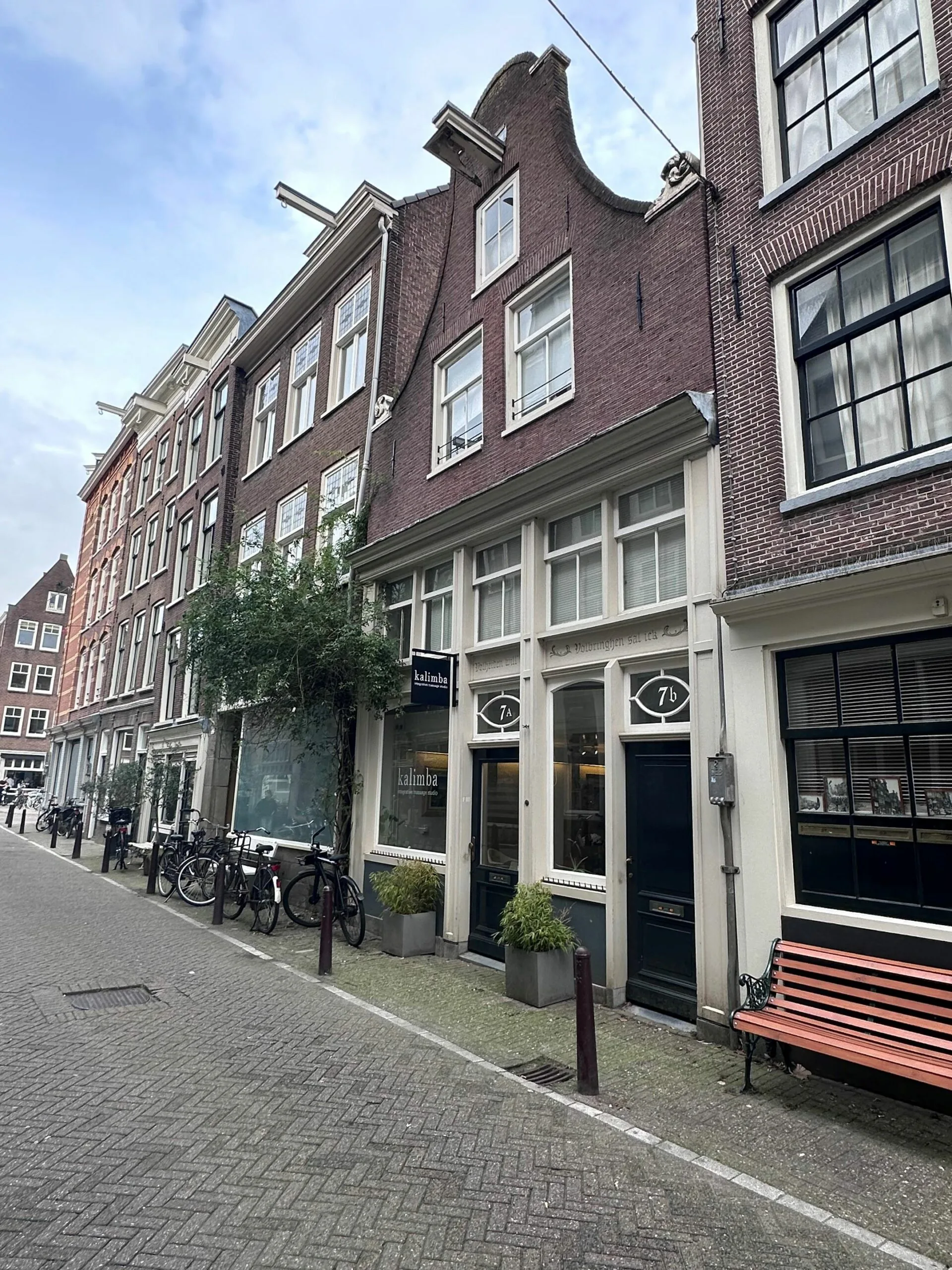 Voorgevel van een smal Amsterdams grachtenpand met het bord van winkel 'Kalimba' en meerdere fietsen op de stoep.