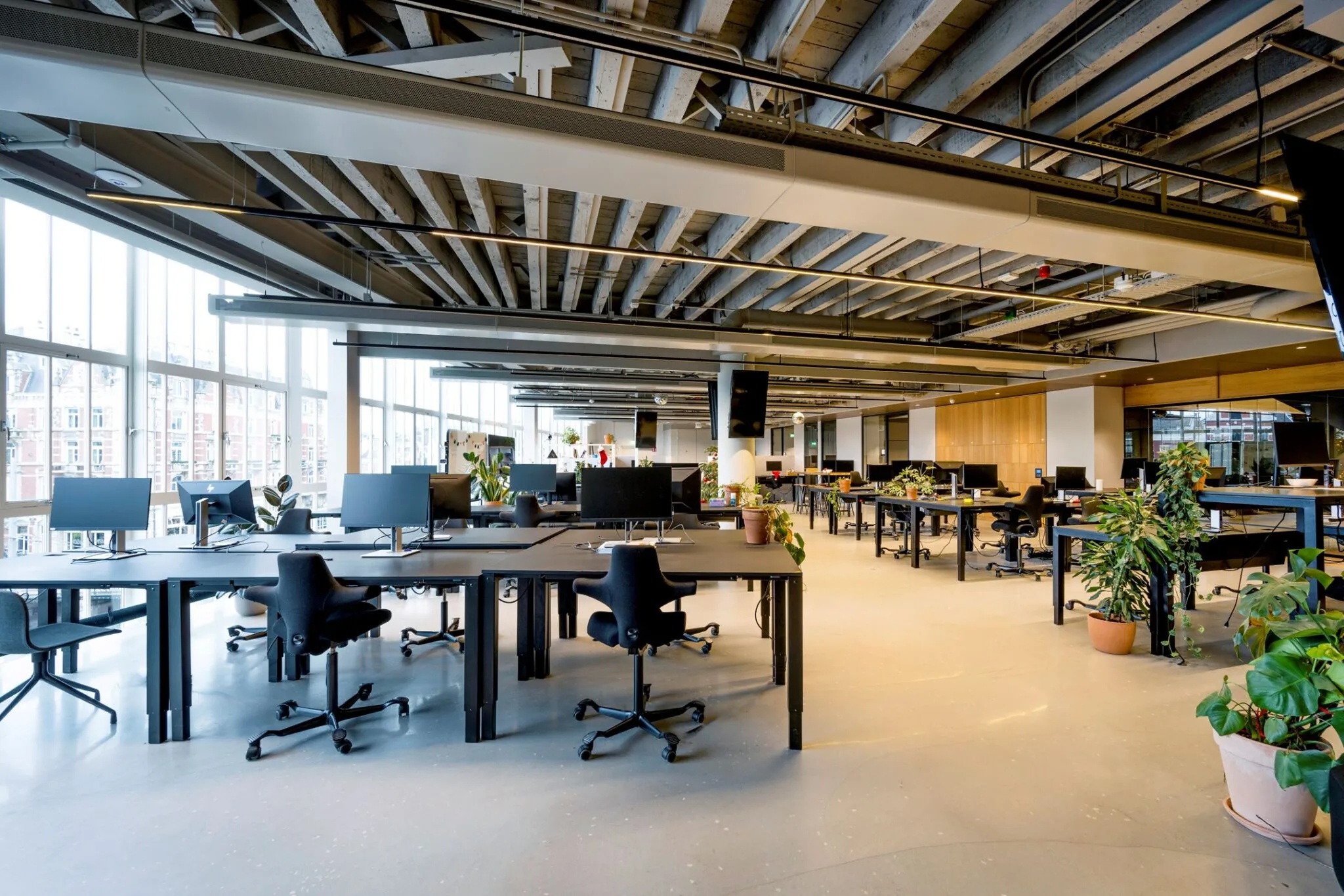 Moderne open kantoorruimte met bureaus, computers en veel groenplanten.