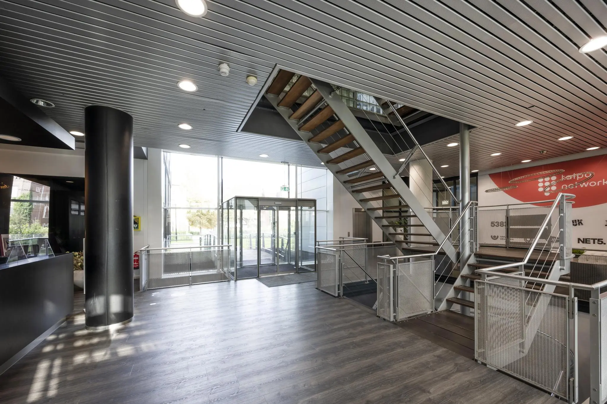 Moderne ontvangsthal van een kantoorgebouw aan het Rietlandpark met houten trap en glazen entree.