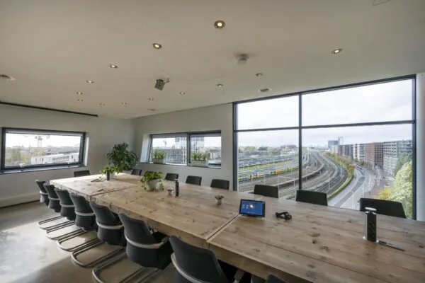 Vergaderruimte met houten tafel en uitzicht op het spoor en gebouwen bij Rietlandpark in Amsterdam.