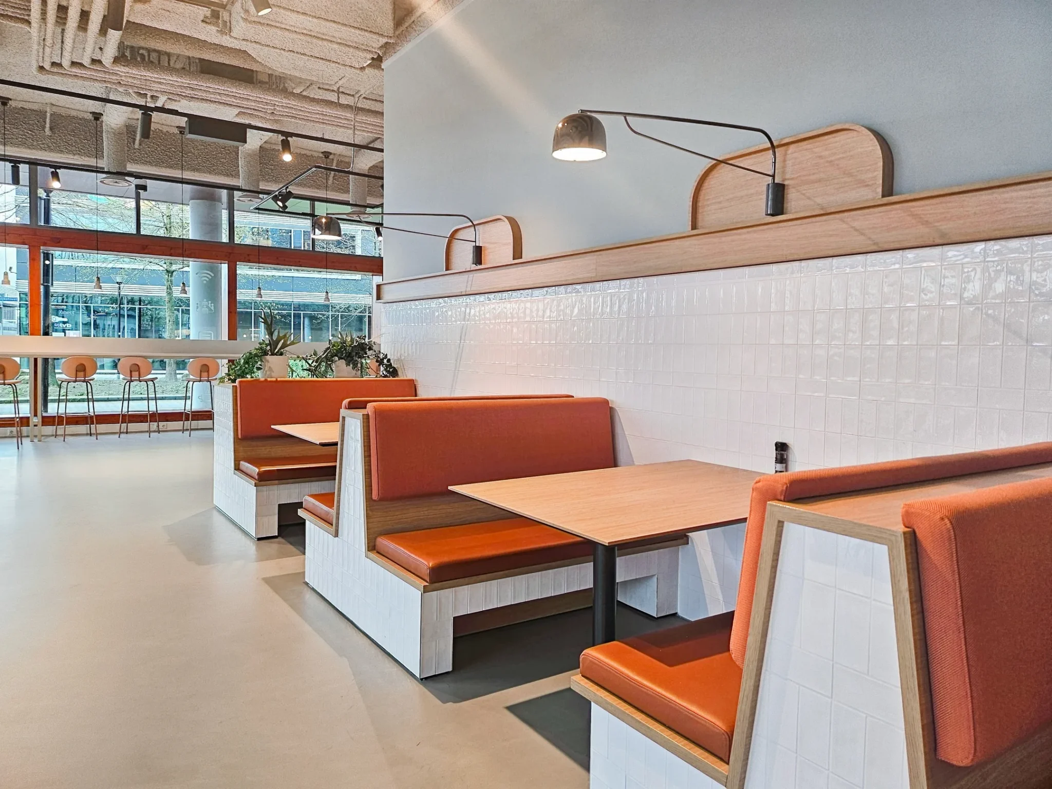 Moderne zithoeken met oranje bekleding en houten tafels in een licht en ruim restaurantinterieur.