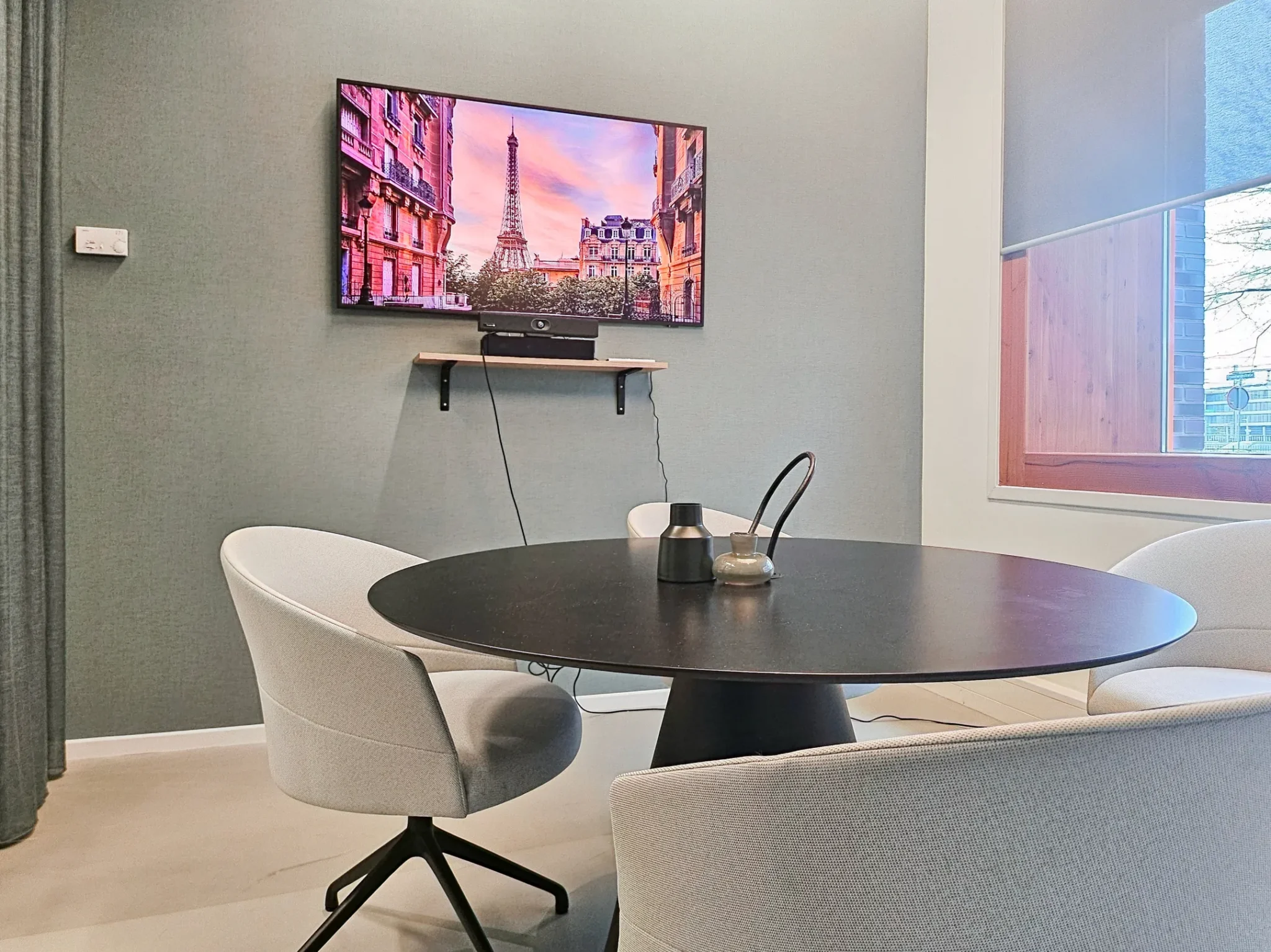 Moderne vergaderruimte met ronde tafel, vier stoelen en een tv-scherm met een afbeelding van de Eiffeltoren.