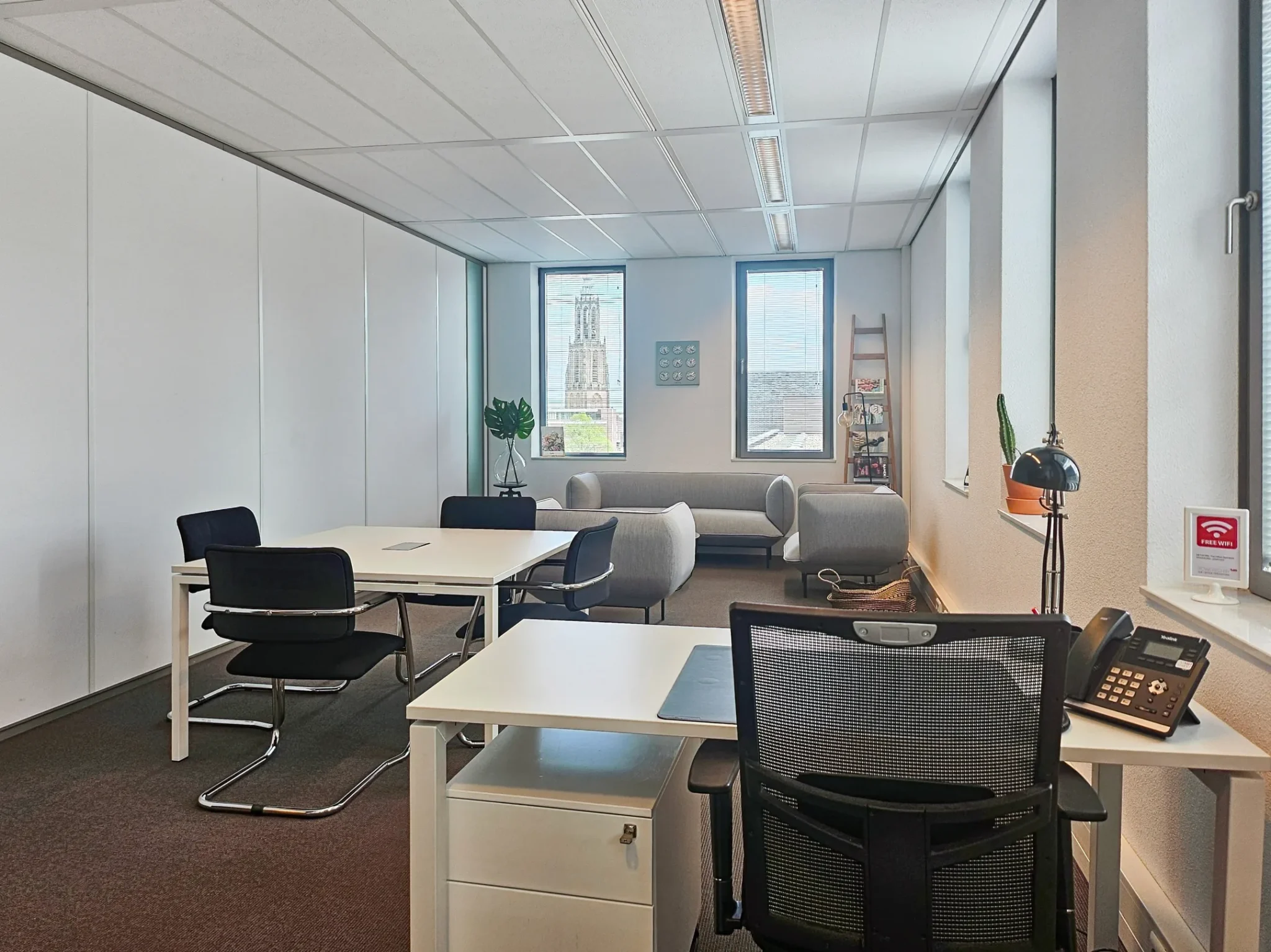 Moderne kantoorruimte met bureaus, vergadertafel, zithoek en uitzicht op de Domtoren door het raam.