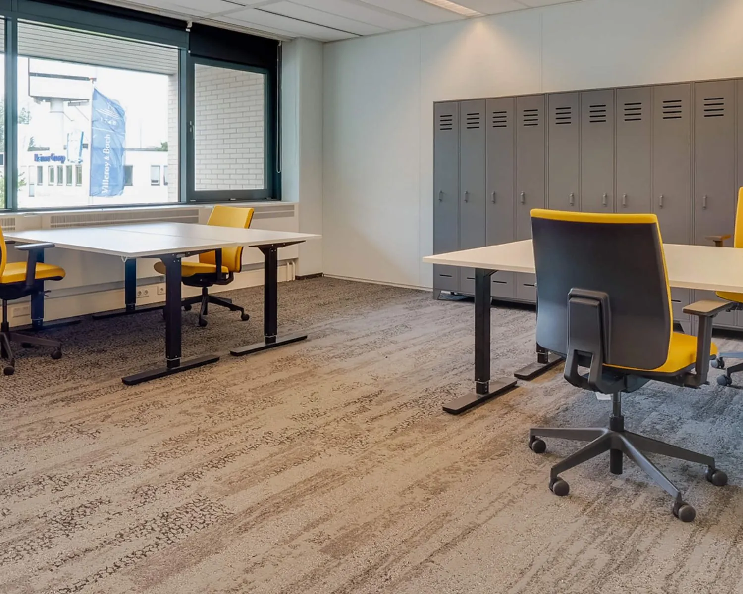 Modern kantoor met bureaus, gele bureaustoelen en een wand met grijze lockers.
