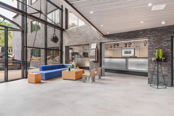 Moderne ontvangstruimte met een blauwe bank, houten tafels en een balie in een gebouw met grote ramen.