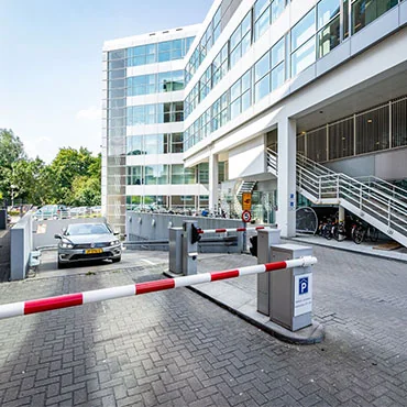 Ingang van een moderne kantoorgebouw met slagboom en parkeergarage.
