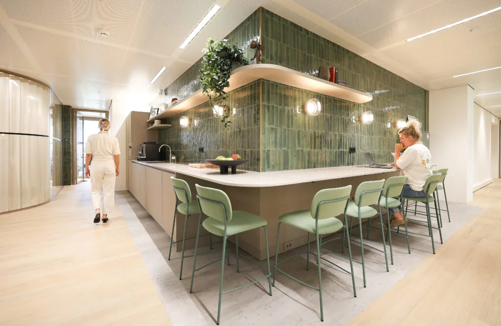Moderne kantoorkeuken in Co-Office Valley Amsterdam met groene wandtegels, barkrukken en werkende personen.