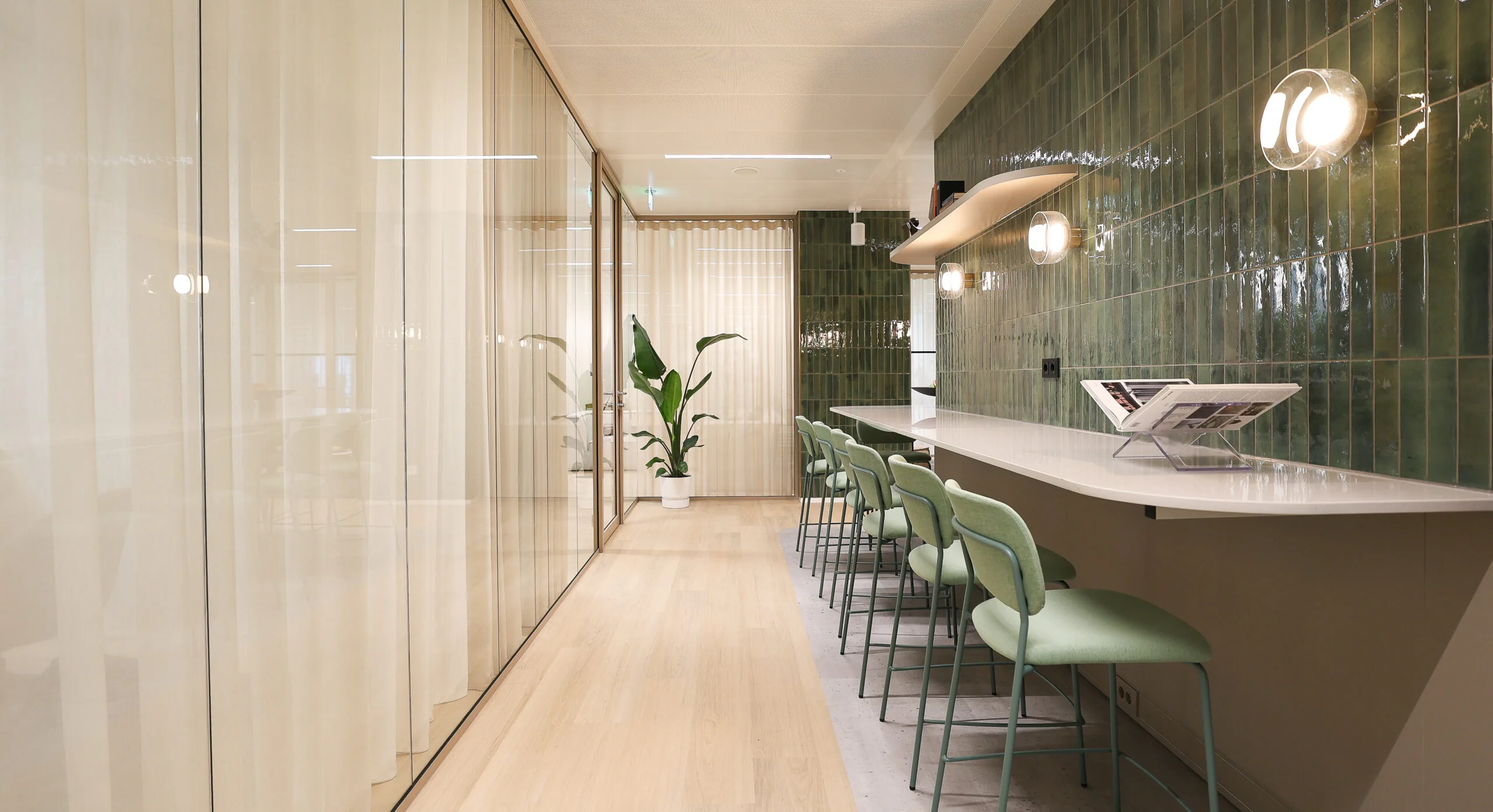 Moderne werkruimte in Co-Office Valley Amsterdam met groene wandtegels, barkrukken en een lange werktafel.