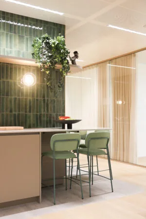 Moderne kantoorkeuken in Co-Office Valley Amsterdam met groene barkrukken, een fruitschaal en een groene betegelde muur.
