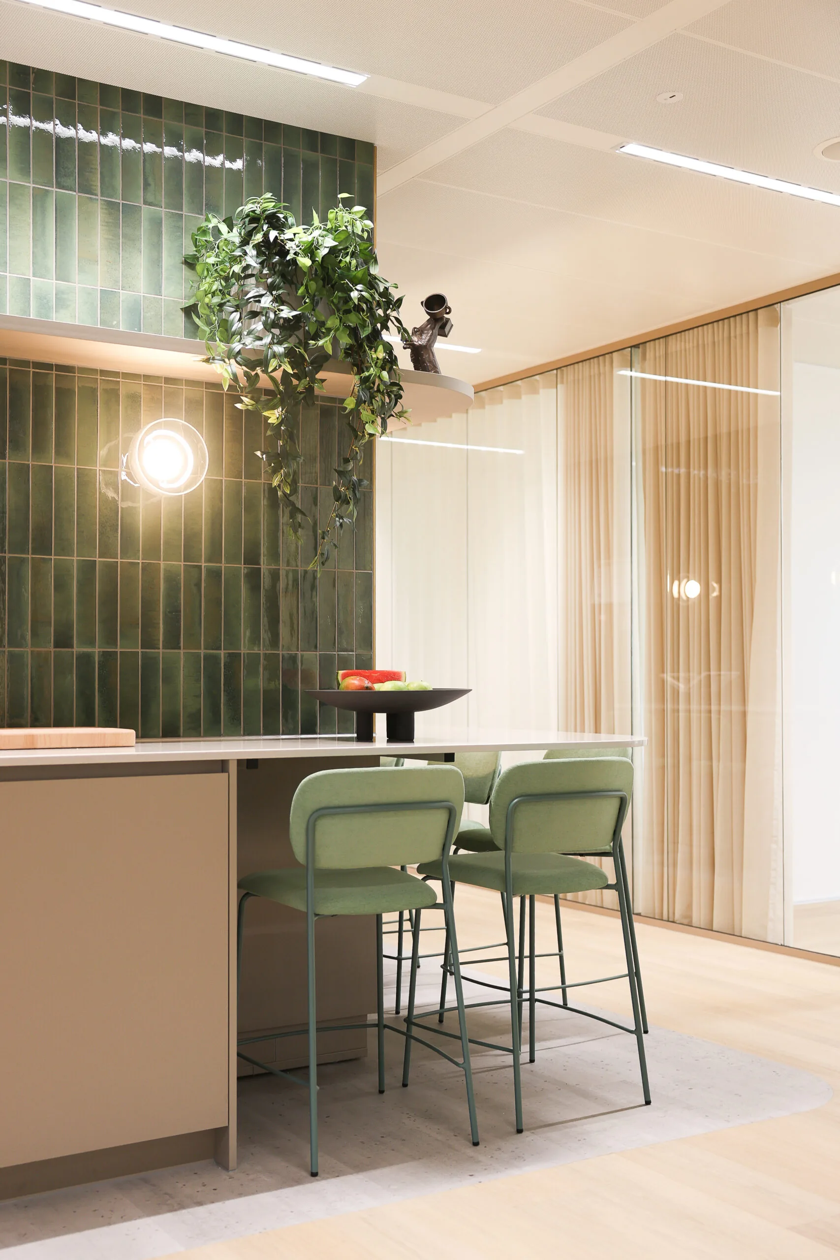 Moderne kantoorkeuken in Co-Office Valley Amsterdam met groene barkrukken, een fruitschaal en een groene betegelde muur.