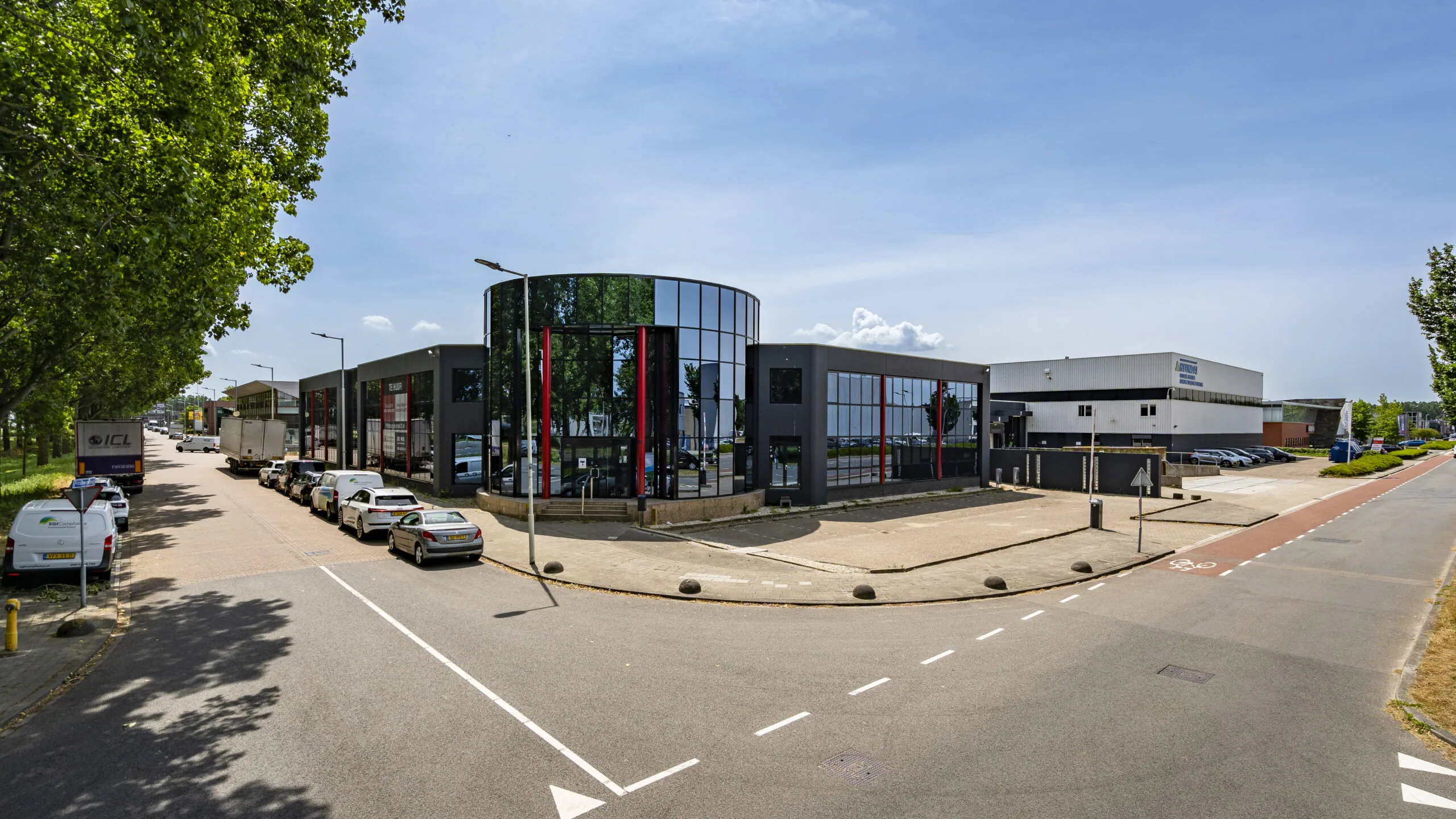 Modern bedrijfsgebouw met glazen gevel en parkeerplaatsen aan een rustige industriële straat.