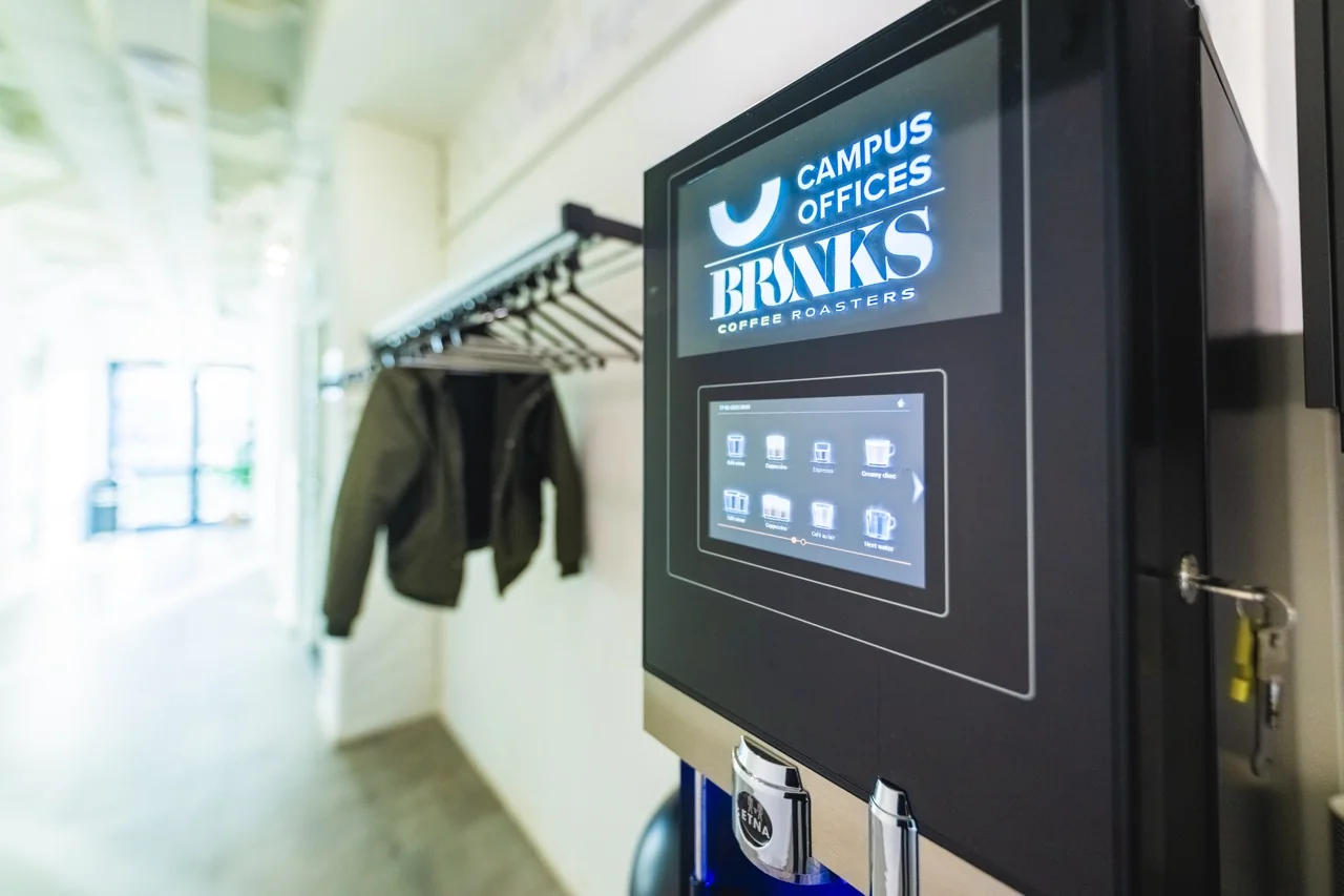 Koffiemachine van BRNKS Coffee Roasters in een lichte gang met kapstok en jas.