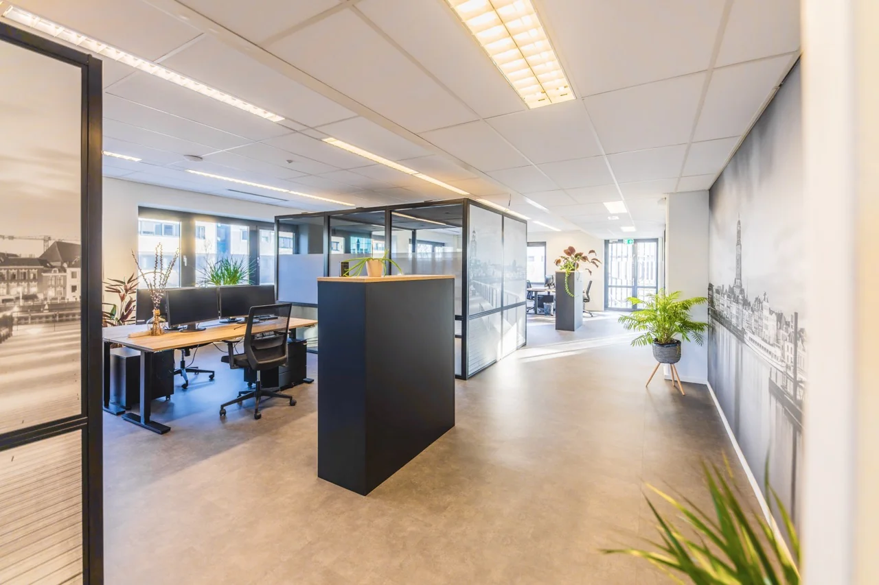 Moderne en lichte kantoorruimte met werkplekken, glazen wanden en decoratieve planten.