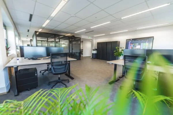 Moderne open kantoorruimte met bureaus, computerschermen, glazen vergaderruimtes en groene planten.