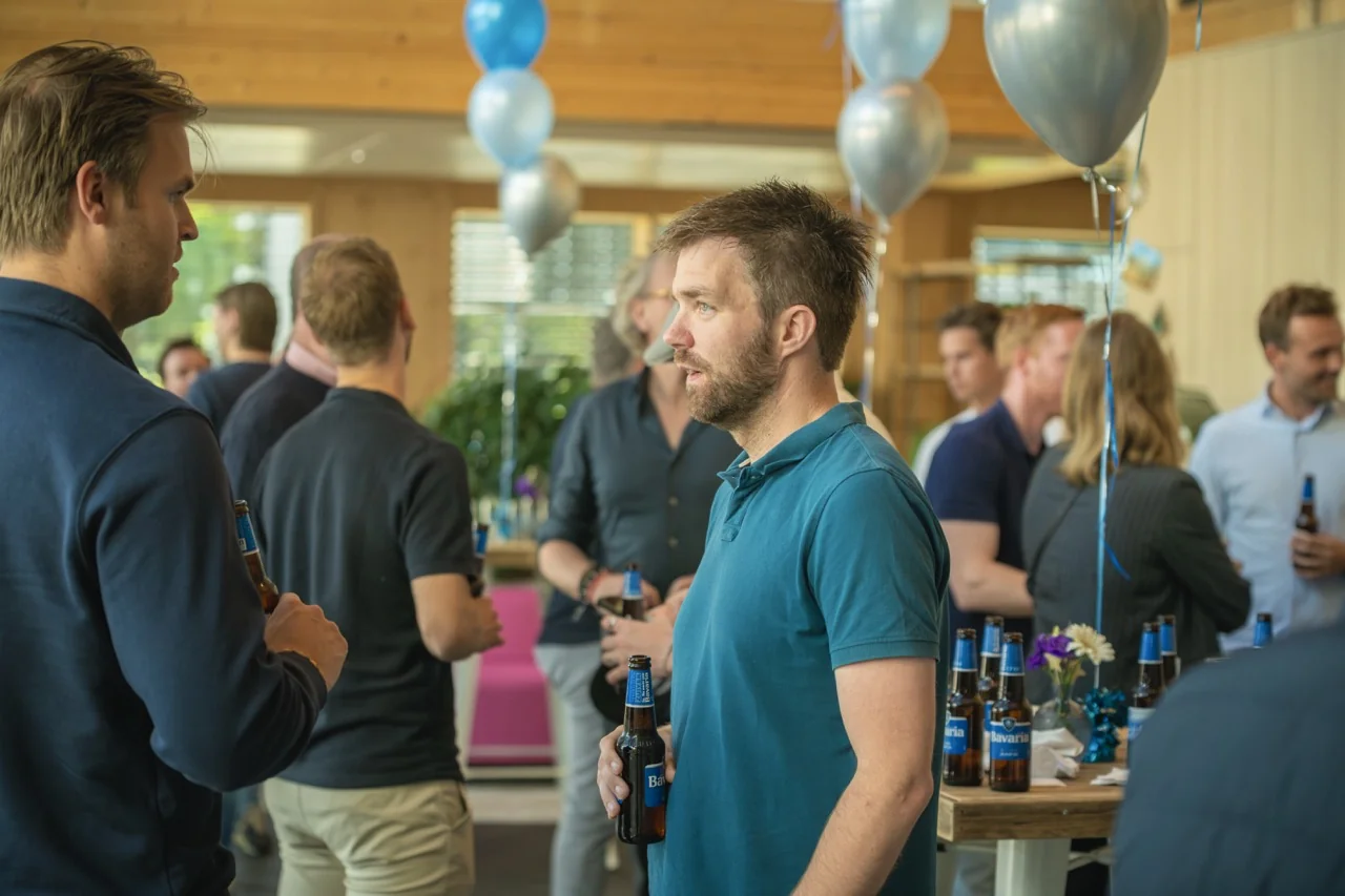 Mensen praten en drinken bier tijdens een informeel feest met ballonnen en decoratie.