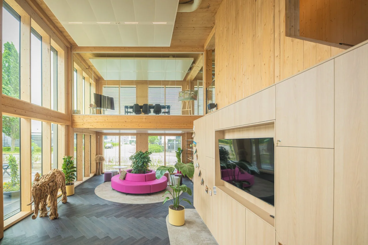 Lichte, moderne kantoorruimte met houten interieur, grote ramen, een roze ronde bank en een decoratief houten olifantenbeeld.