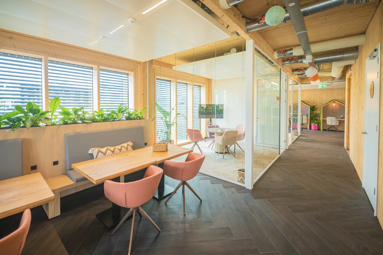Modern, licht en duurzaam ingericht kantoor met houten elementen, glazen vergaderruimtes en groene planten.