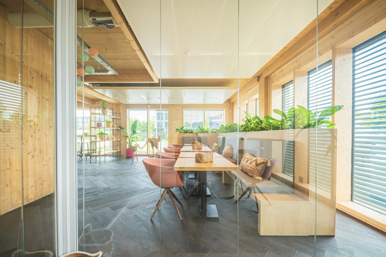 Moderne vergaderruimte met houten interieurelementen, veel daglicht en groene planten.