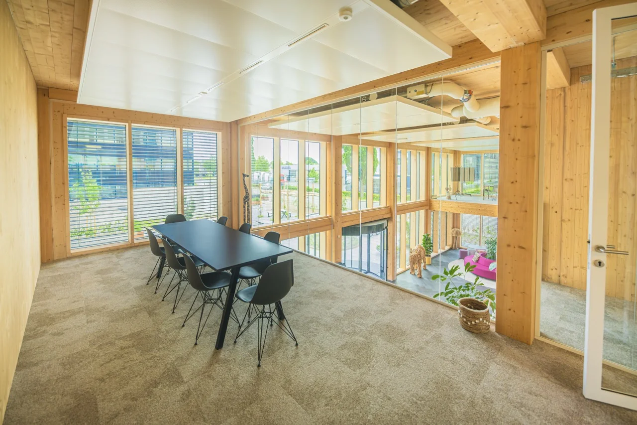 Vergaderruimte met houten wanden, glazen wanden en uitzicht op een open, licht atrium met moderne inrichting.