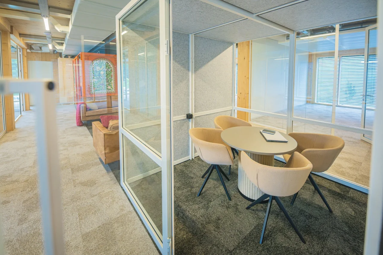 Vergaderruimte met vier beige stoelen rond een ronde tafel in een modern kantoorinterieur met glazen wanden.