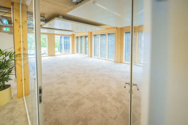 Licht en leeg kantoor met houten accenten, grote ramen en beige tapijt.