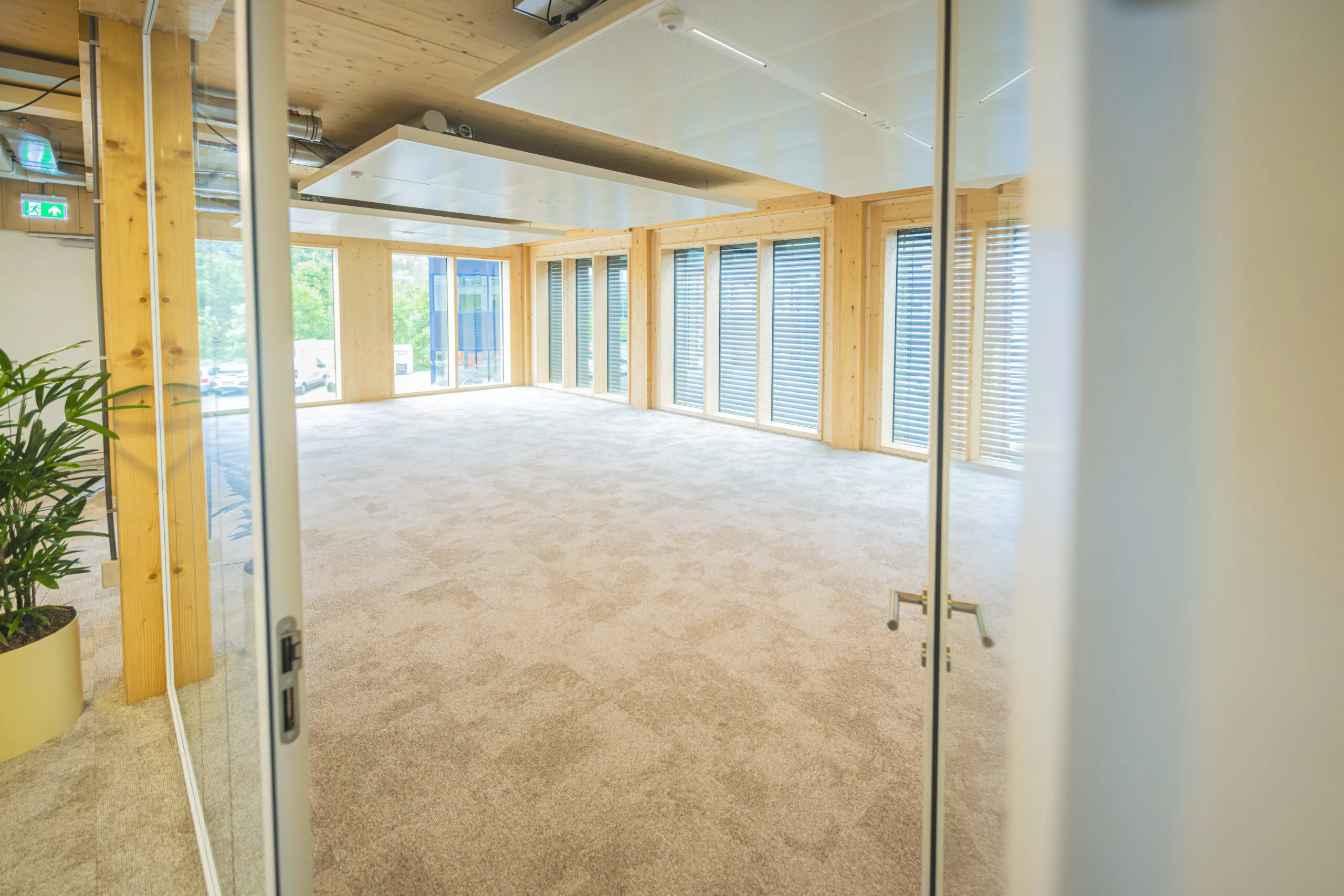 Licht en leeg kantoor met houten accenten, grote ramen en beige tapijt.