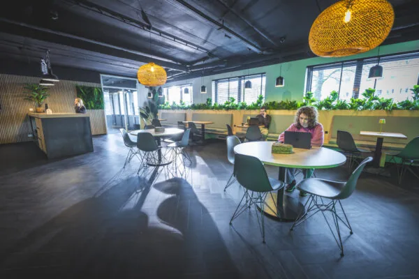 Moderne en sfeervolle lounge- en werkruimte met mensen die op laptops werken aan ronde en vierkante tafels.