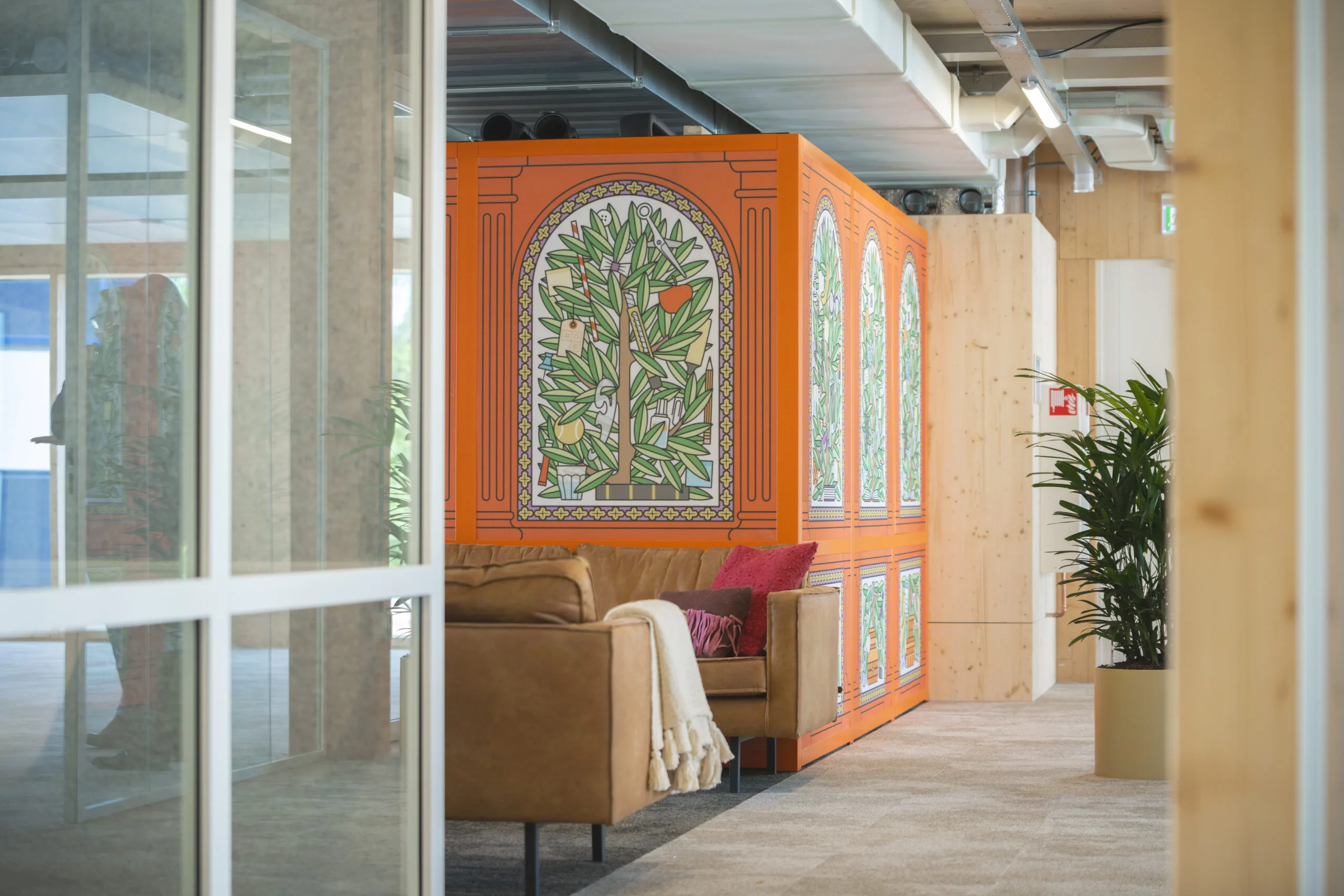 Zithoek met bruine bank en kleurrijke wand met illustraties van bomen in een modern kantoorinterieur.