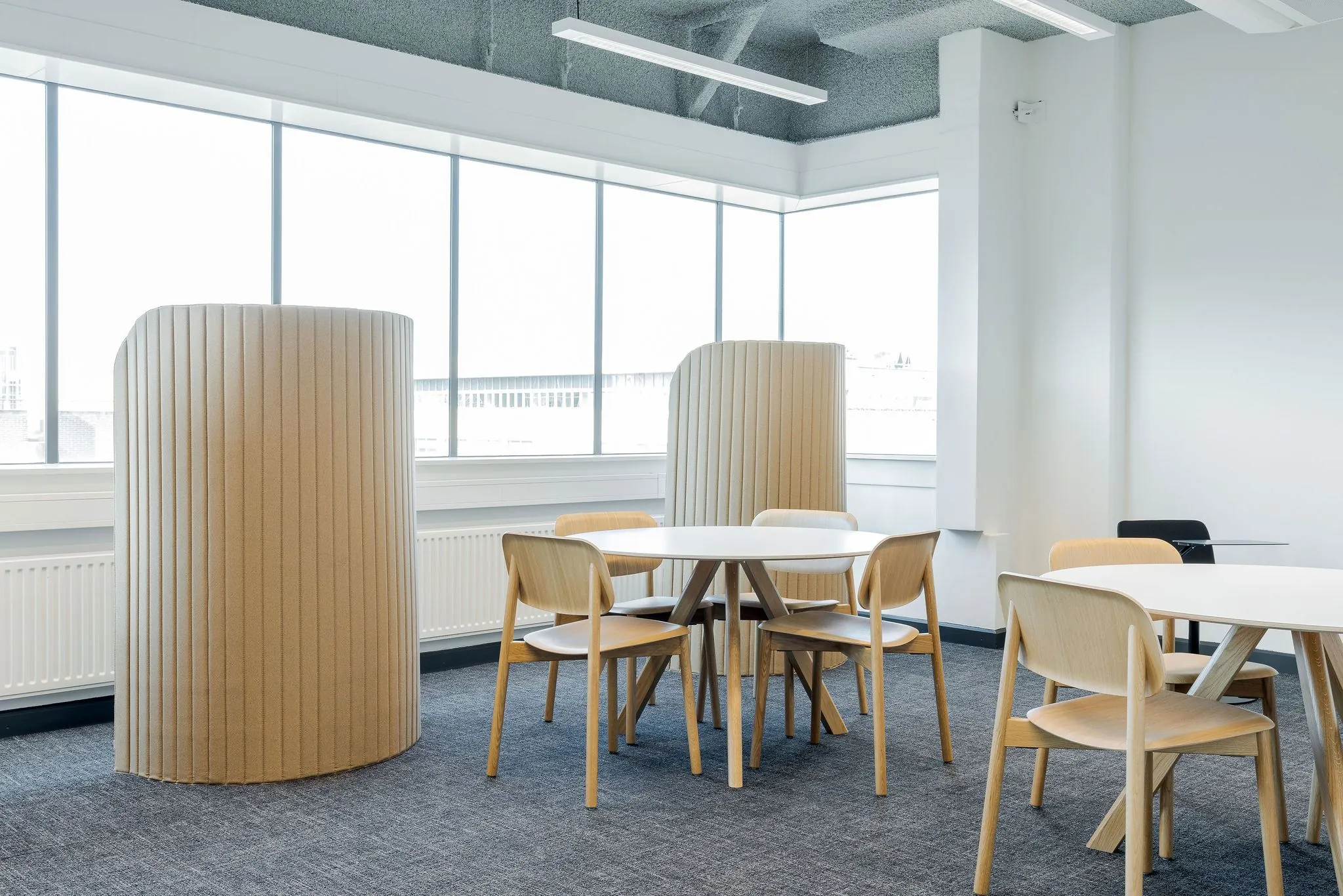 Moderne kantooruimte aan de Daalsesingel 51 met houten stoelen, ronde tafels en akoestische panelen bij grote ramen.