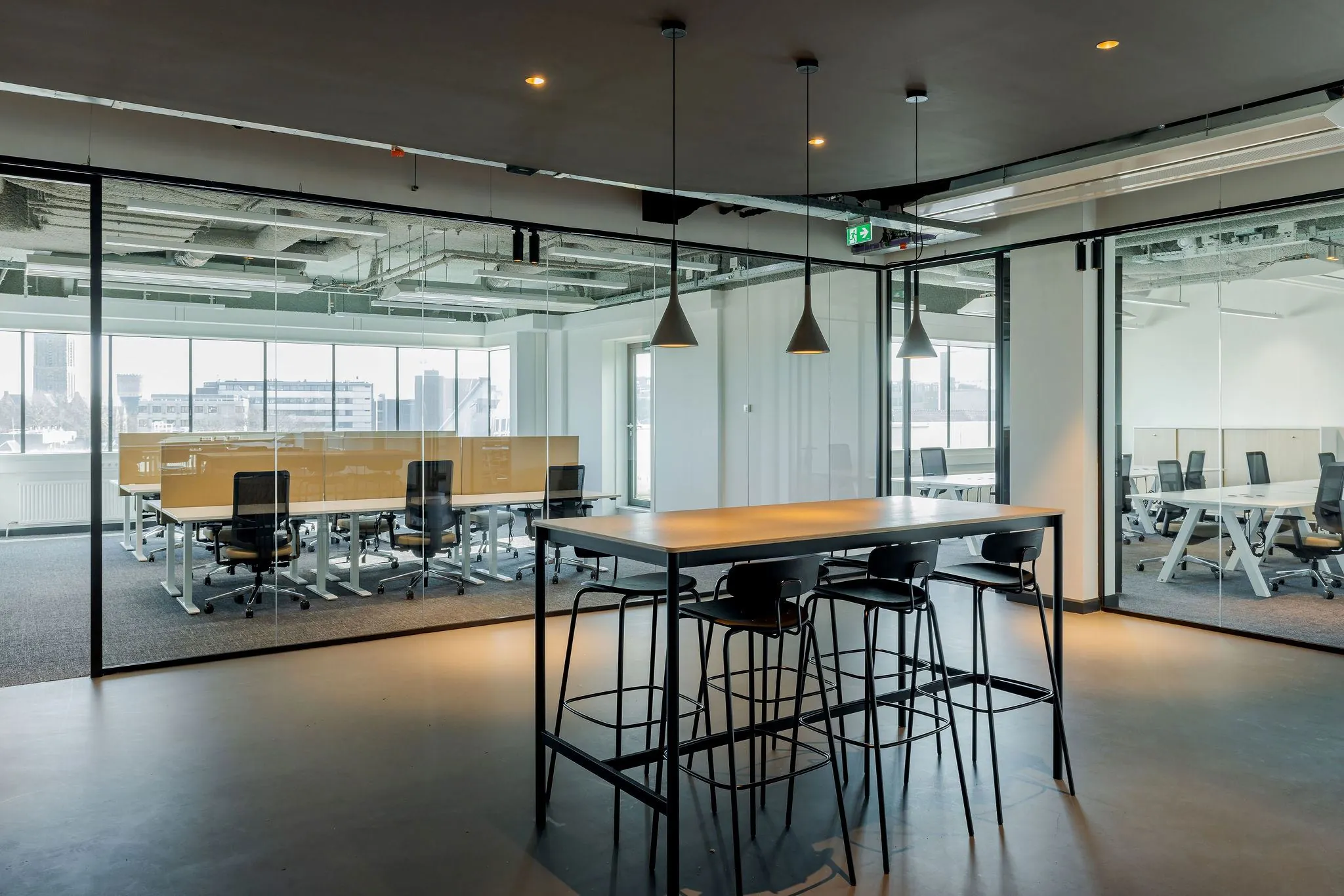 Moderne kantoorruimte aan de Daalsesingel 51 met glazen wanden, werkplekken en een hoge tafel met barkrukken.