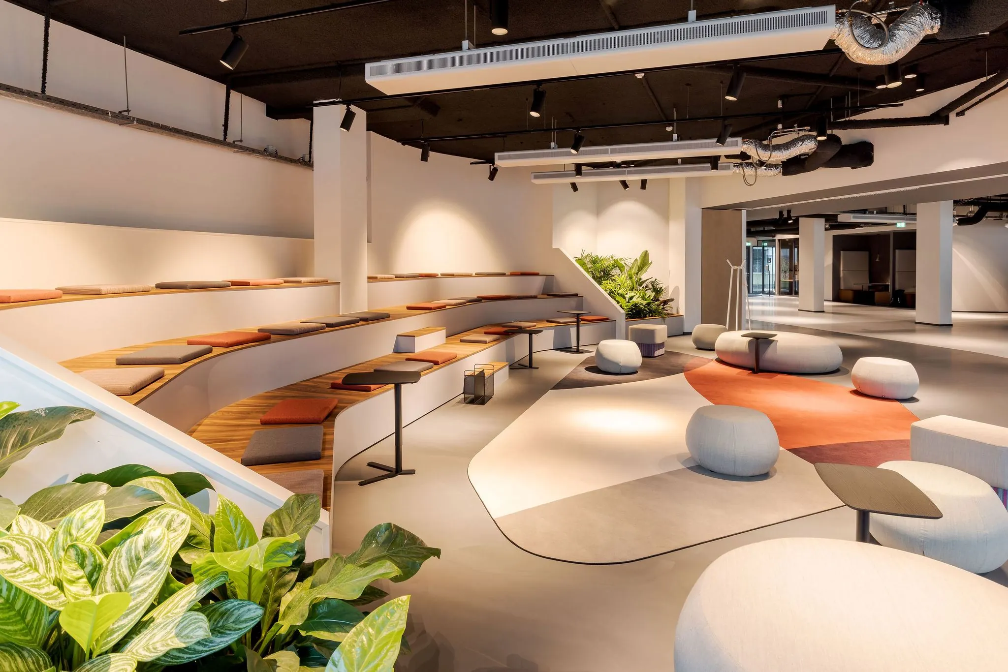 Moderne en open kantoorlounge aan de Daalsesingel 51 met tribunezitplaatsen, zachte poefjes en veel natuurlijke elementen.