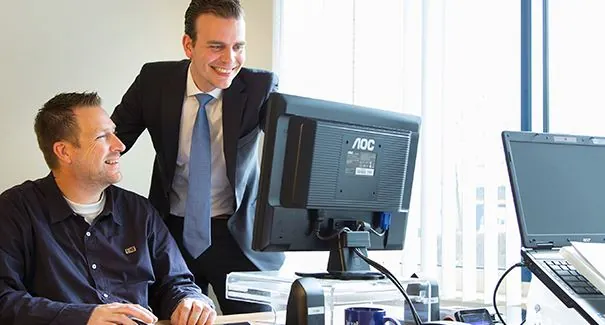 Twee mannen werken samen achter een bureau met computerschermen op een kantoor aan de Dr. Nolenslaan 157.