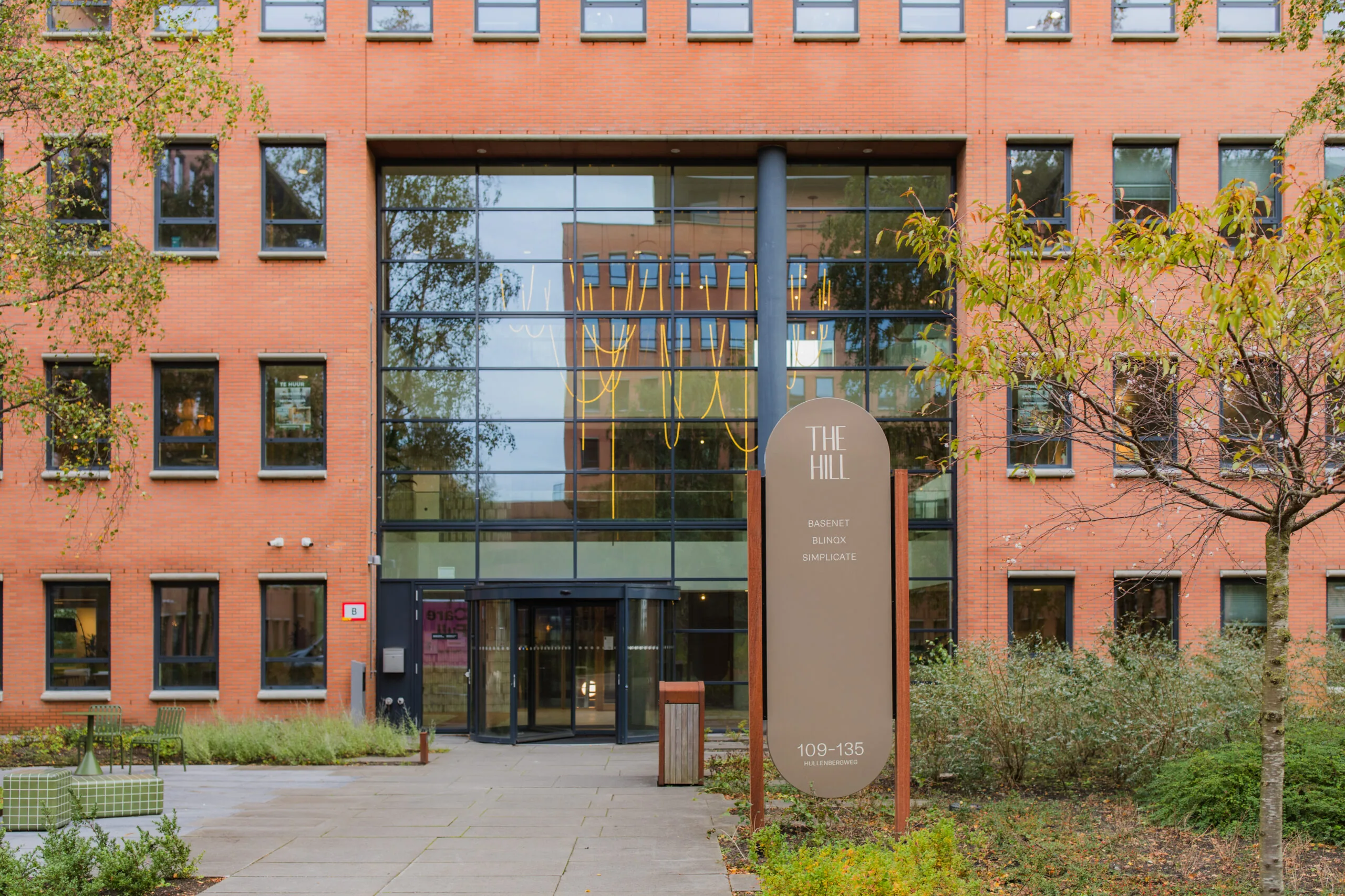 Front entrance of The Hill office building at 109–135 Hullenbergweg with a glass facade and company sign.