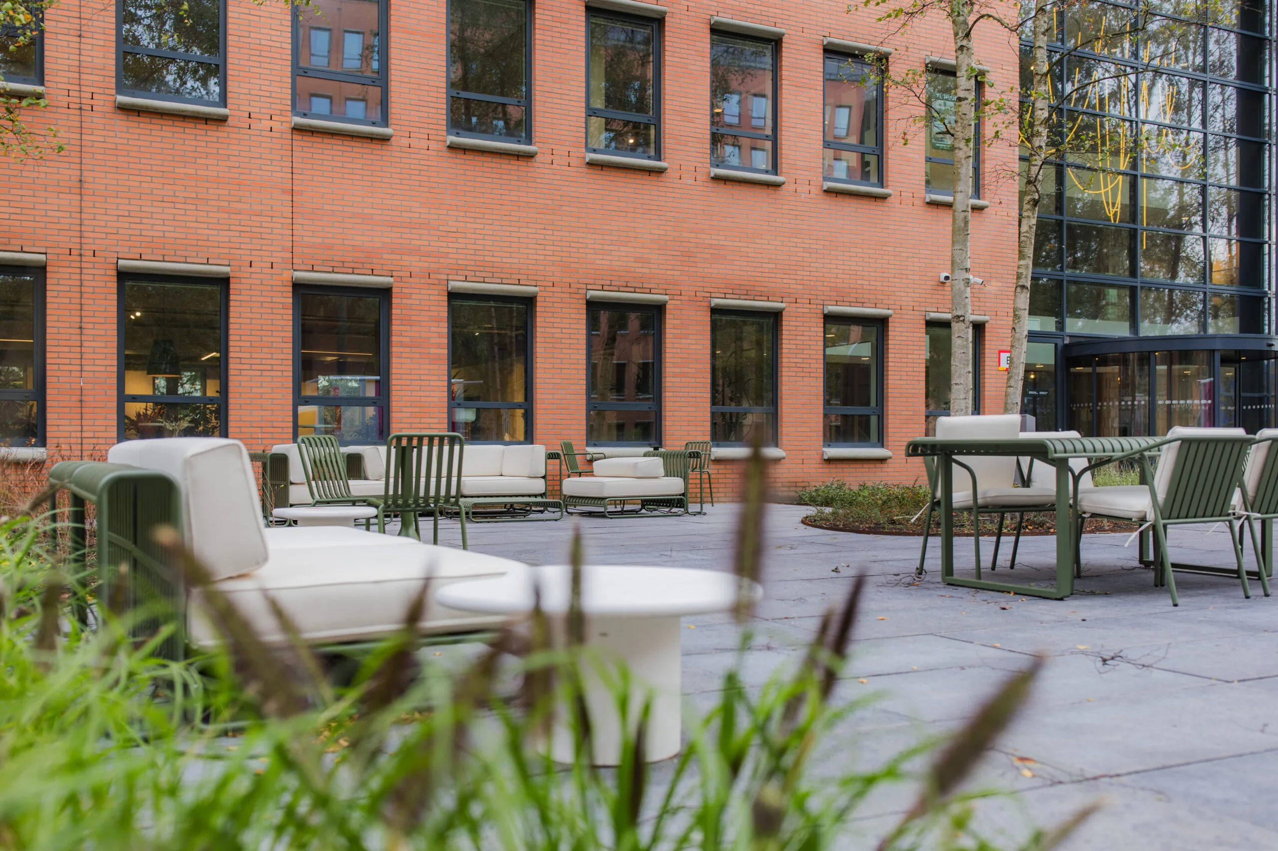 Outdoor seating area with modern furniture in front of the Hullenberg building with a brick facade and large windows.