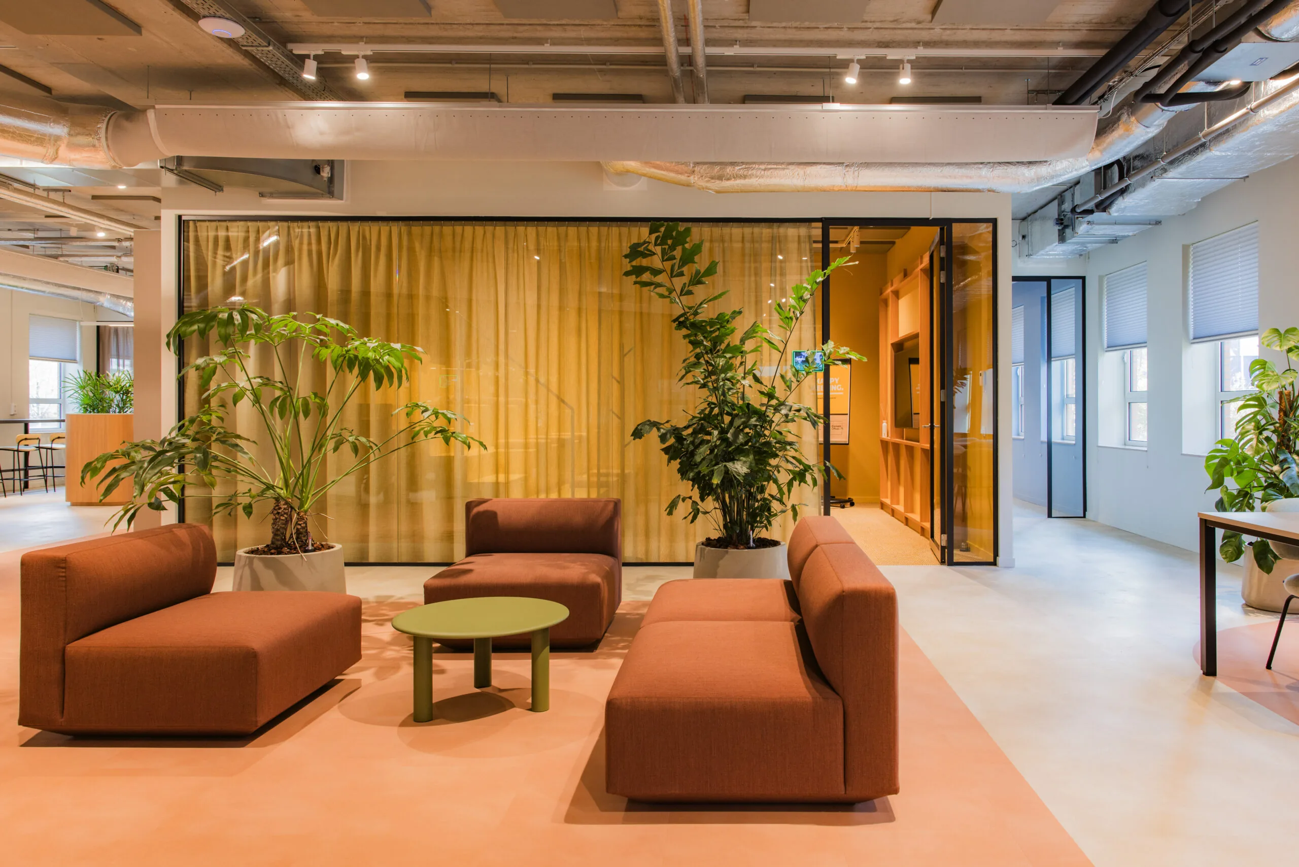 Modern office lounge area in Hullenberg with terracotta seating, green plants, and warm-toned decor.