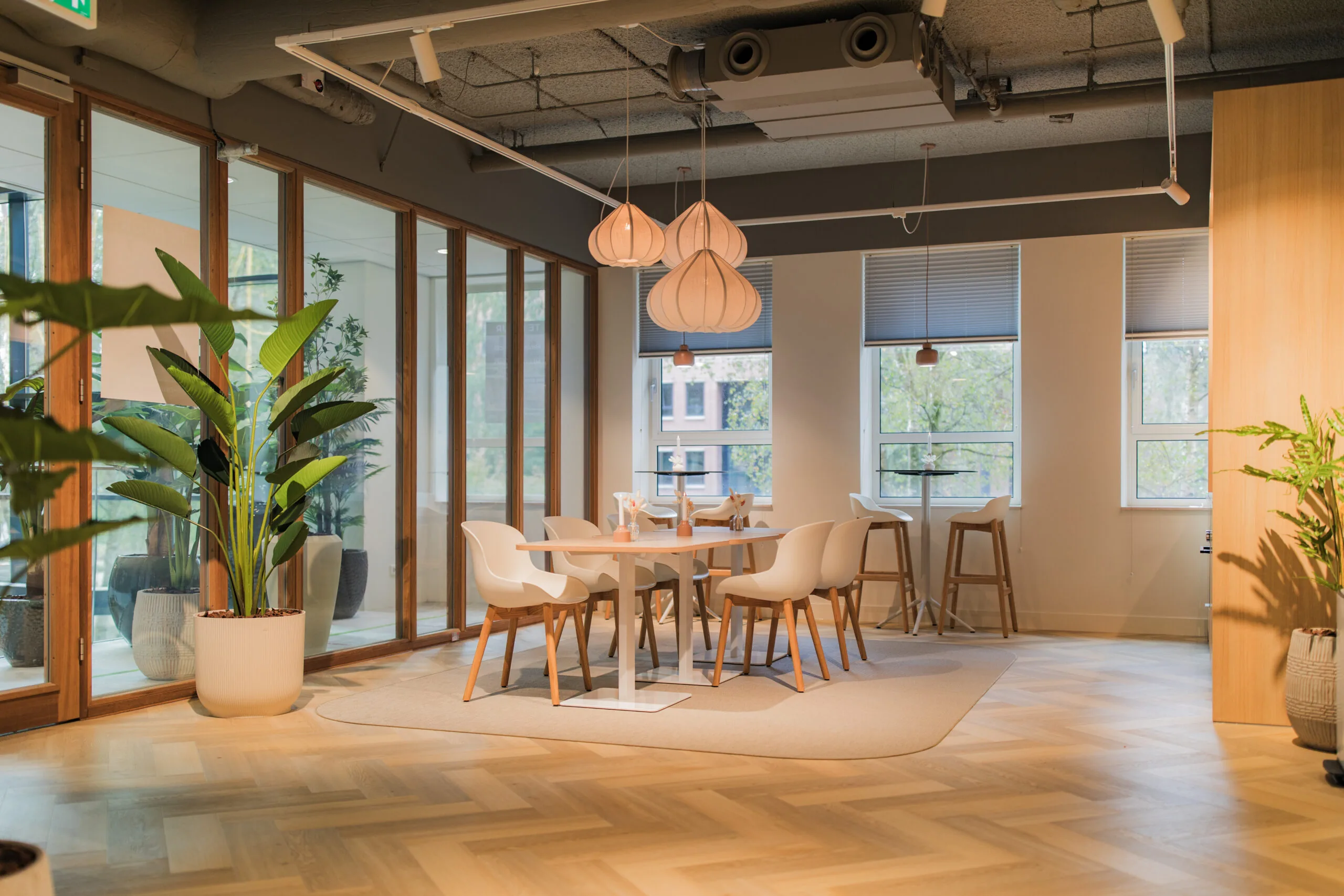 Modern office lounge area at Hullenberg 125 with wooden flooring, stylish seating, and large indoor plants.