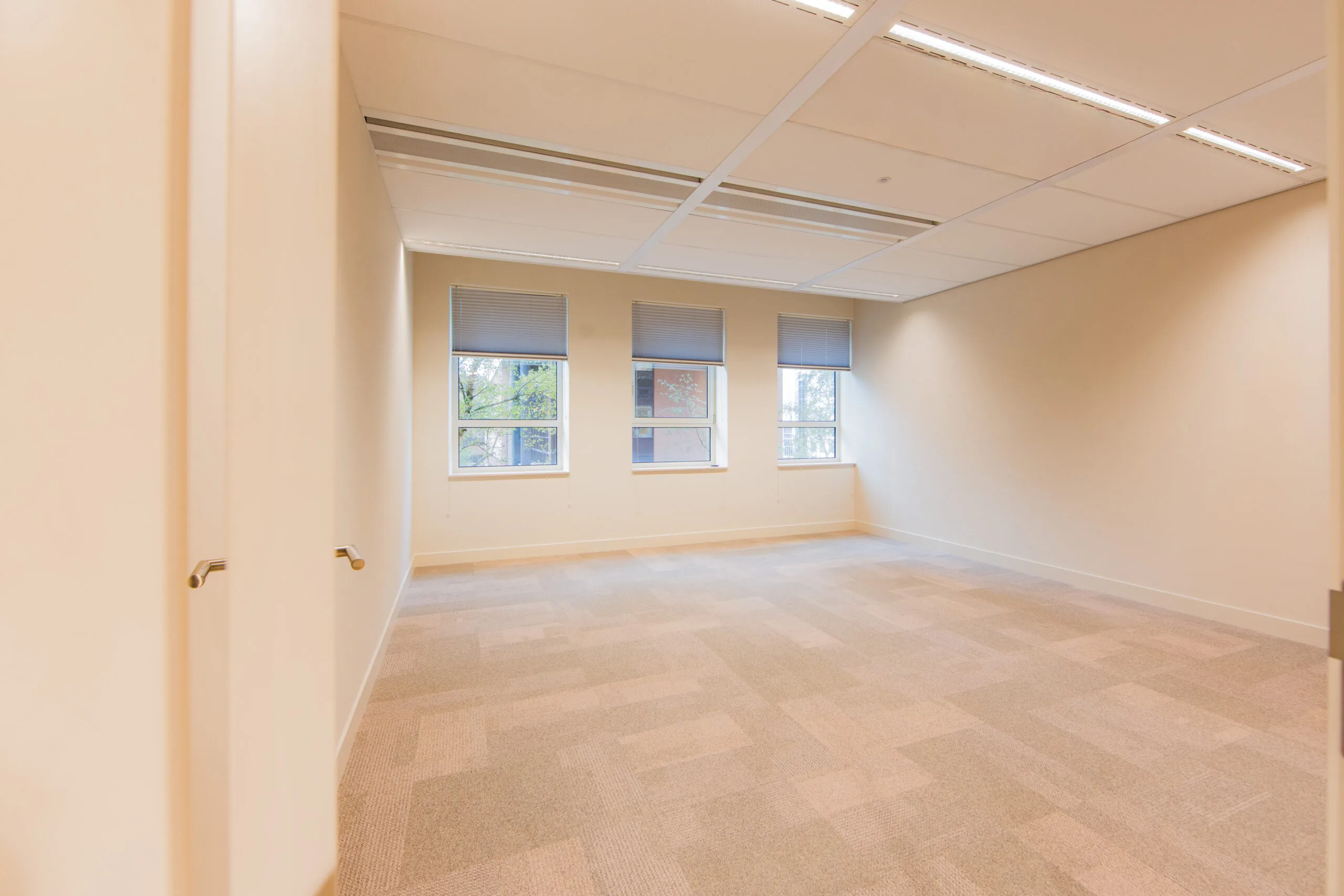 Empty office space at Hullenberg 132 with beige carpet, white walls, and three windows with blinds.