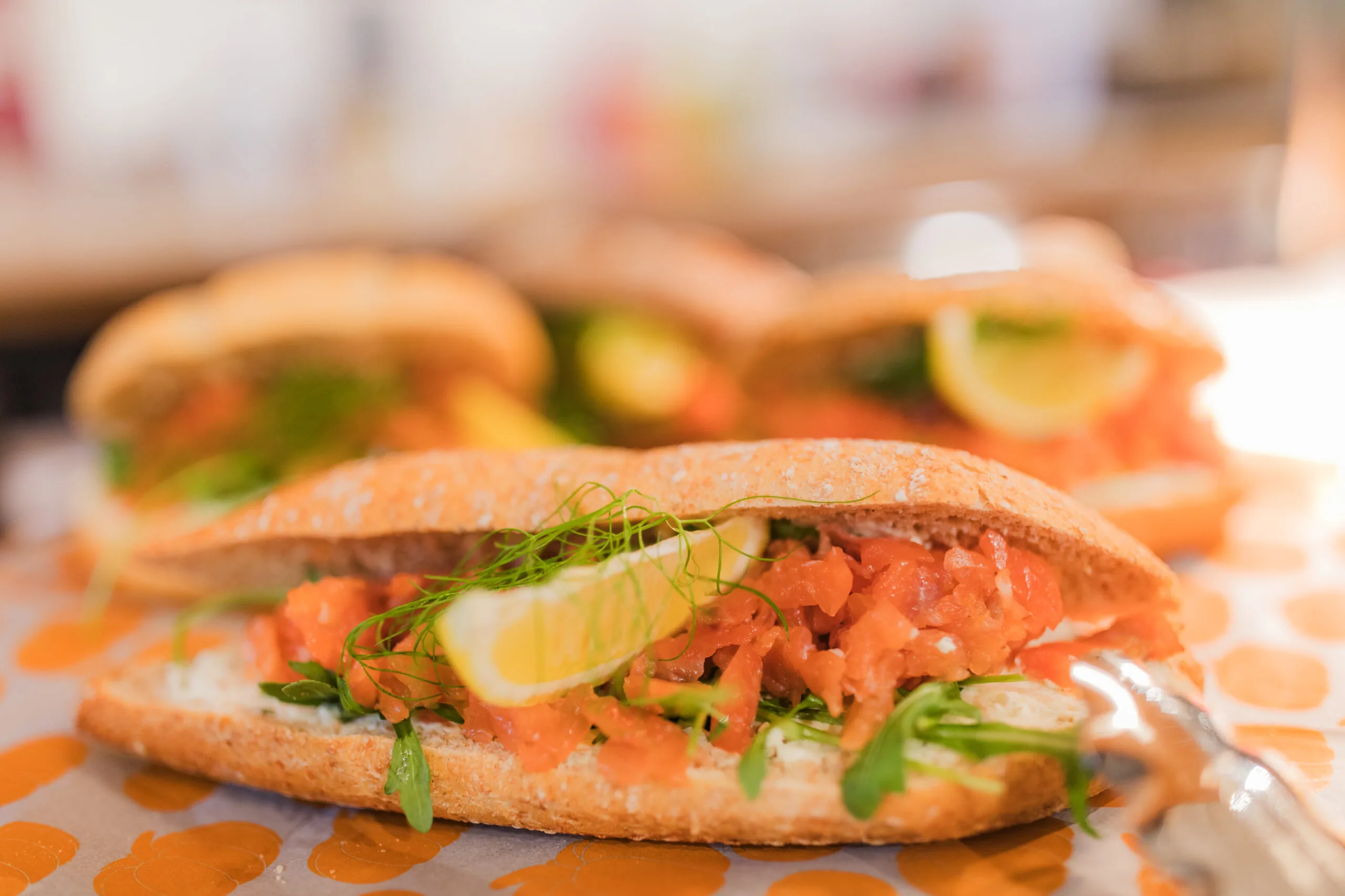 Close-up of fresh sandwiches filled with salmon, cream cheese, arugula, dill, and a lemon wedge on top.