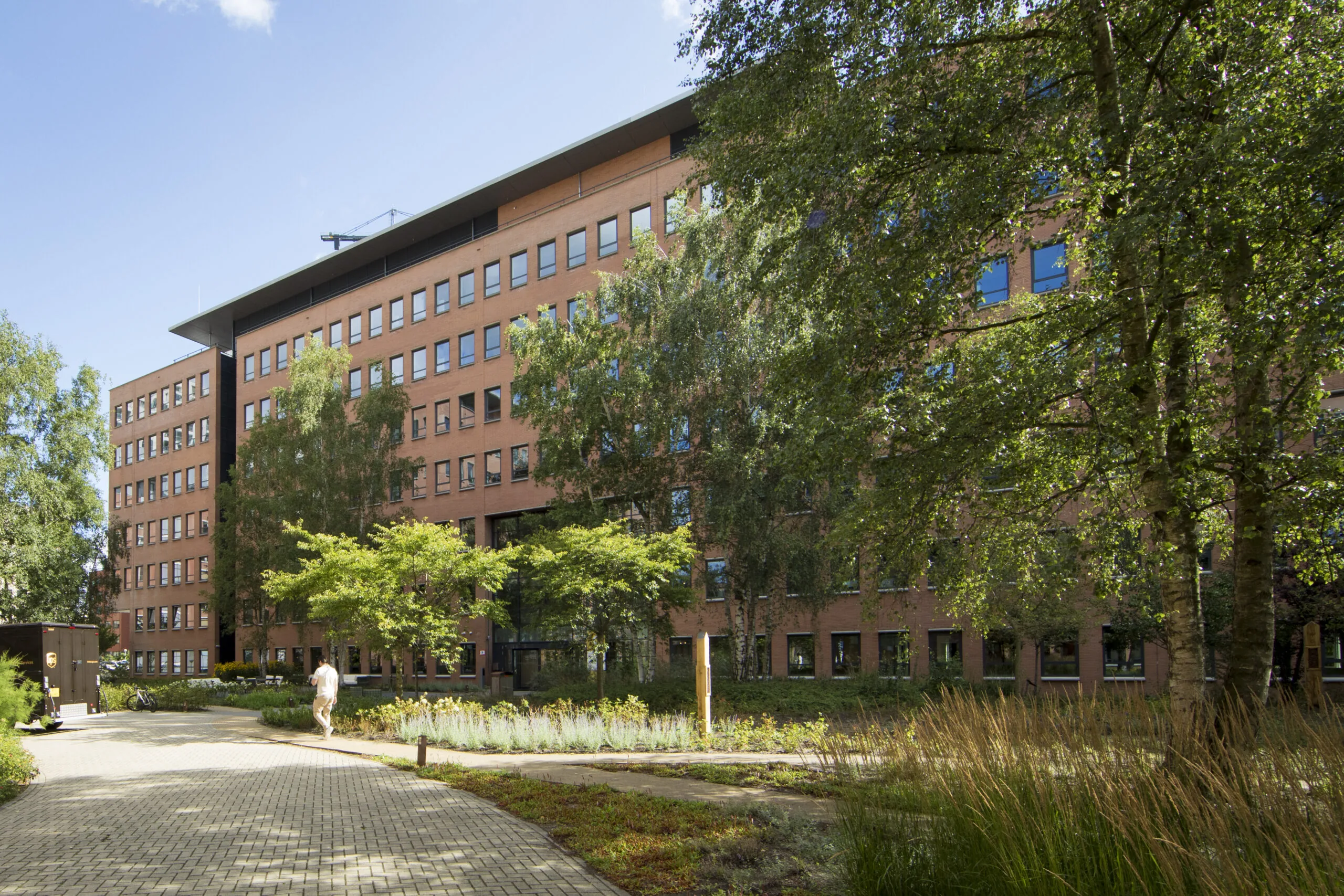 A modern red-brick office building named EO-ADHUL01 surrounded by trees and greenery on a sunny day.