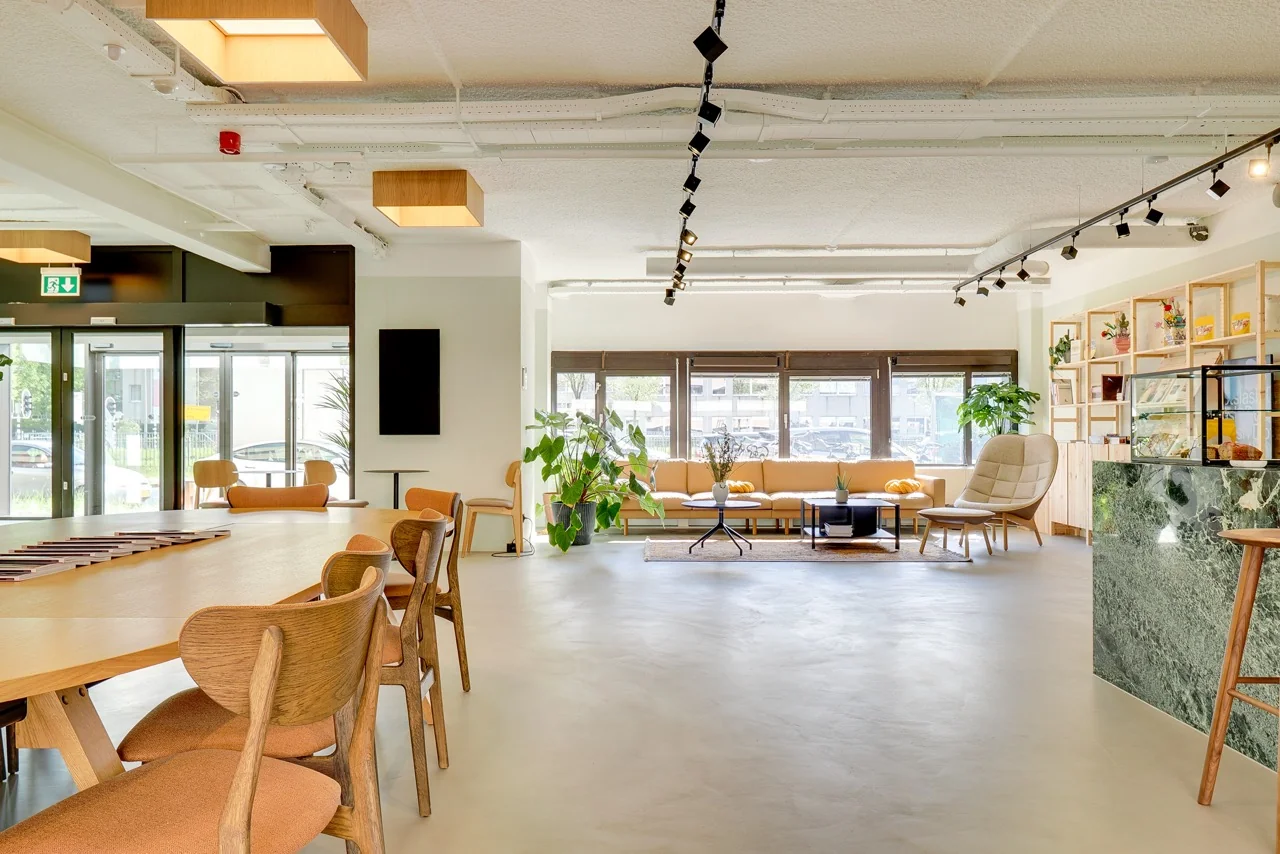 Moderne, lichte ontvangstruimte op Europalaan 93 met houten meubels, een gele zithoek en veel planten.
