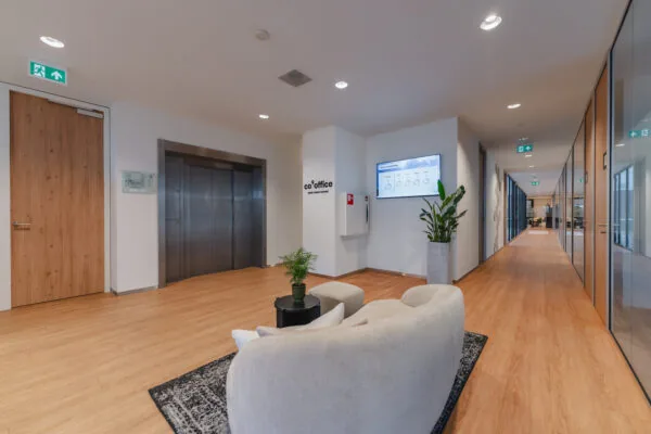 Moderne gangruimte met zithoek, planten, een lift en glazen kantoorwanden bij co°office.