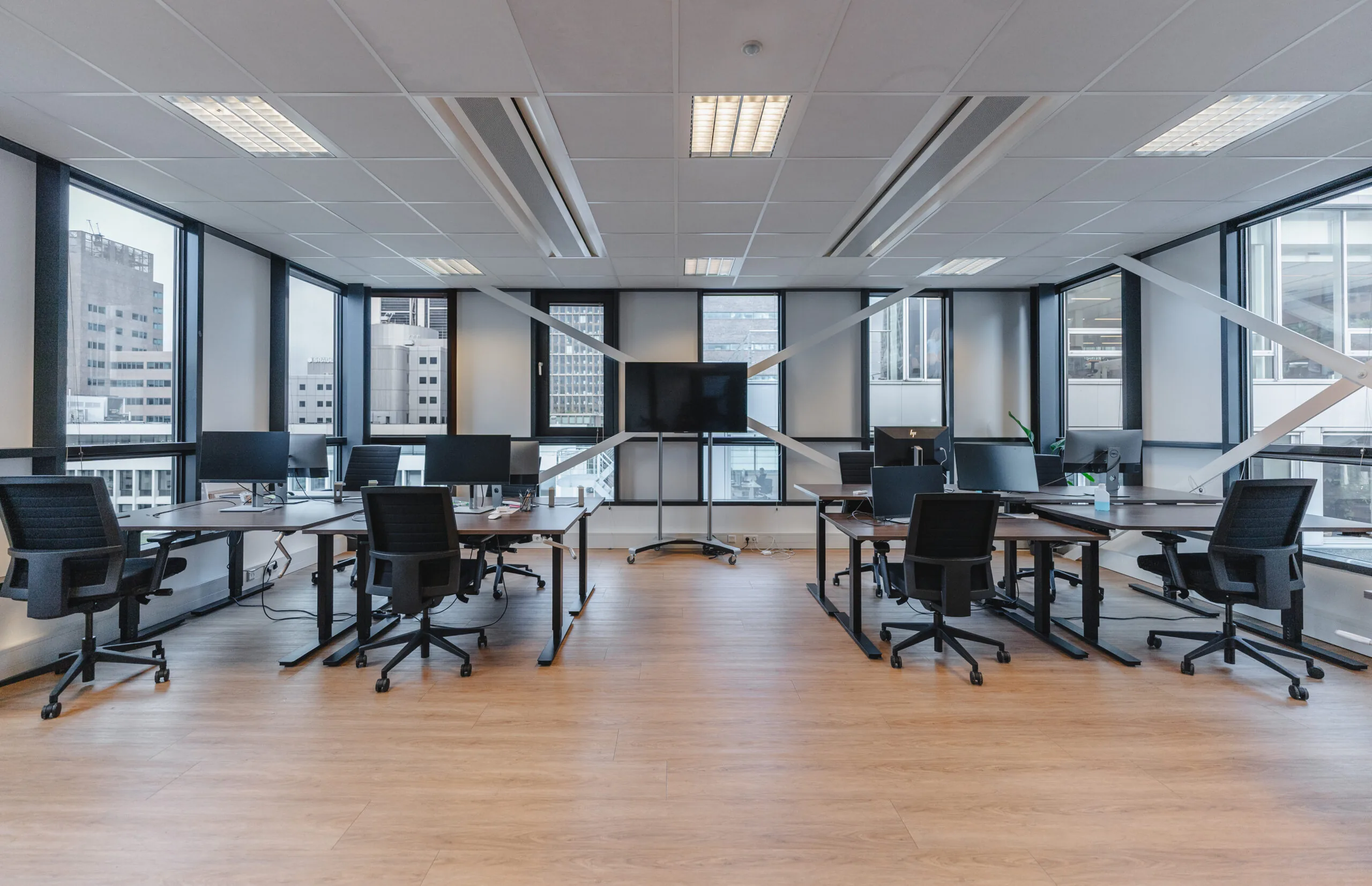 Moderne kantoorruimte met werkplekken, bureaustoelen, computers en een grote monitor, omringd door ramen met uitzicht op de stad.